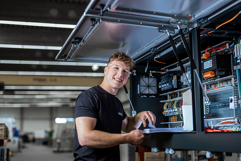 Un empleado del servicio técnico de LoeschPack está delante de un armario eléctrico con una carpeta