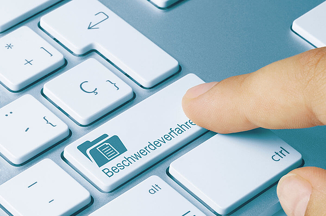 Section of a keyboard with the word complaint procedure on the Enter key and the index finger clicking on it.