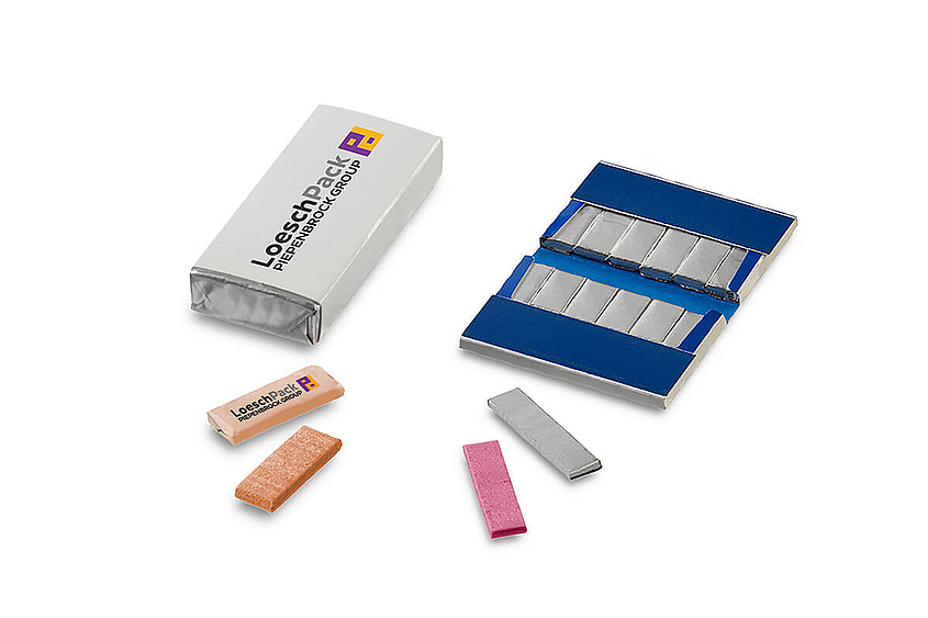 Eine große Kaugummiverpackung liegt neben einer aufgeklappten Verpackung, während im Vordergrund einzelne verpackte Kaugummistreifen zu sehen sind